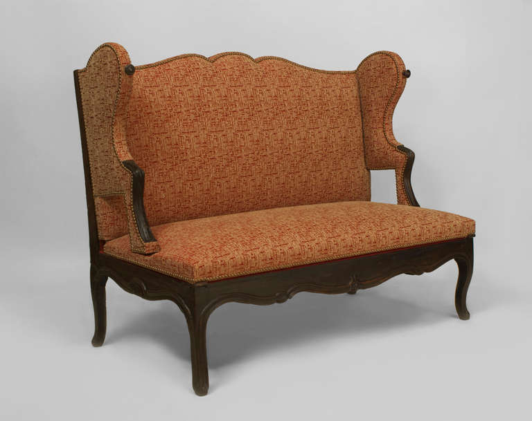 Eighteenth century French Provincial walnut loveseat with an upholstered wing back and seat with short open arms above four cabriole legs and a shaped apron. The loveseat converts into a bed.