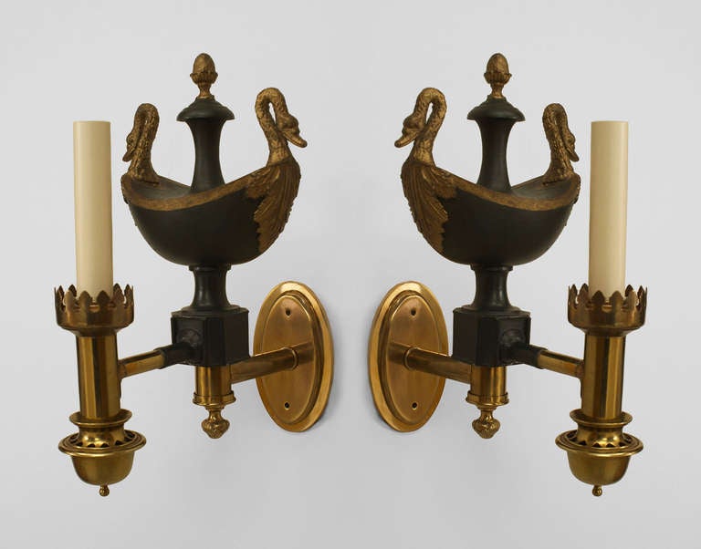 Pair of French Empire electrified wall sconces, each with an elliptical brass bracket with a single brass arm emanating from a green tole oil lamp with gold swan-form handles and a finial top.