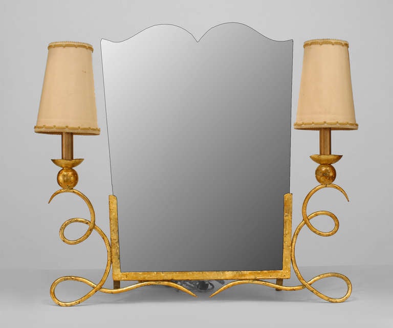 French Art Deco gilt wrought iron dressing table mirror characterized by scroll form sides that support two shaded side lamps and flank a bevelled keystone form mirror. Attributed to Rene Drouet.