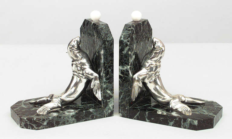 Pair of Art Deco bookends signed Frecourt, each featuring a silver plated  bronze seal propped against a green marble base as if reaching towards a spherical finial carved in imitation of a ball.