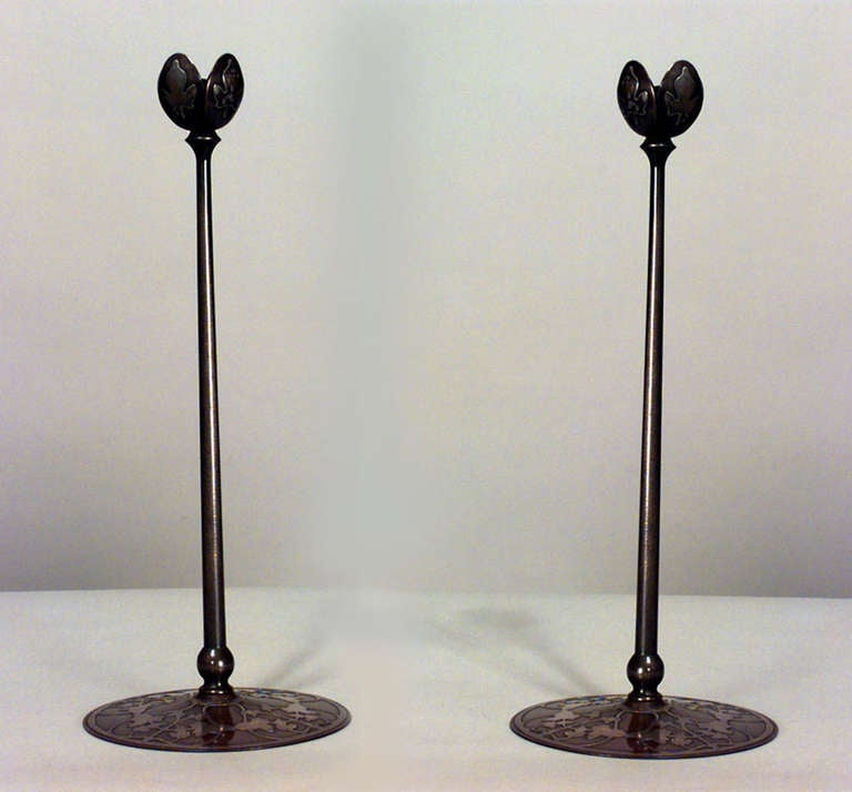 Pair of tall bronze American Mission candlesticks attributed to Heinz Art Metal. These candlesticks are characterized by a brown patina and a floral design in silver deposit at the base and top.