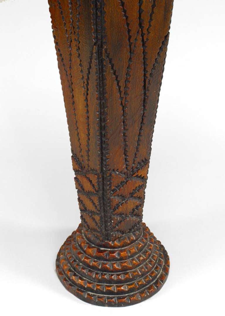 Rustic end table of continental origin. Intricate tramp art style carving dominates this table's surface, including its round top, pine cone apron, and tapered square pedestal form culminating in a tiered round base.
