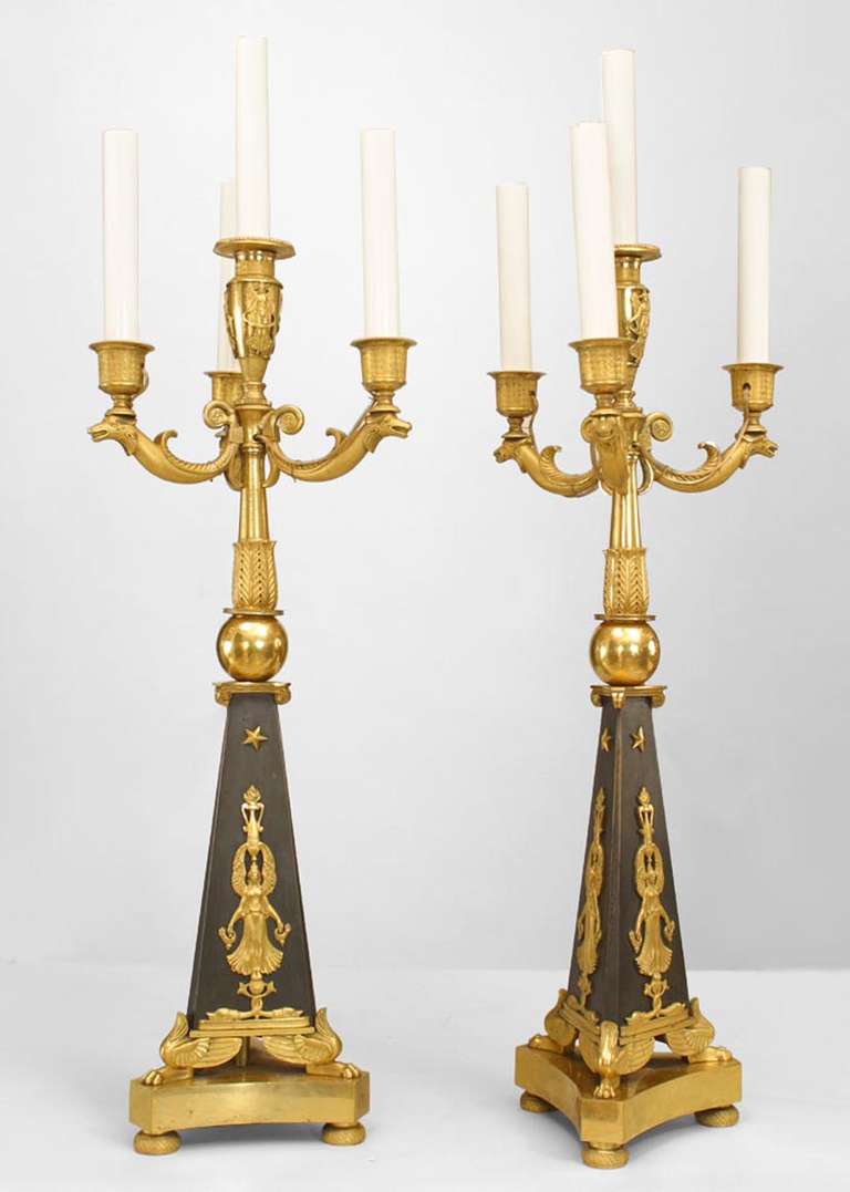 Pair of nineteenth century French Empire style candelabra. Each gilt-trimmed bronze candelabrum features a central urn-top arm surrounded by three bestial arms above a blackened tripartite base decorated with classicizing details, such as stars,