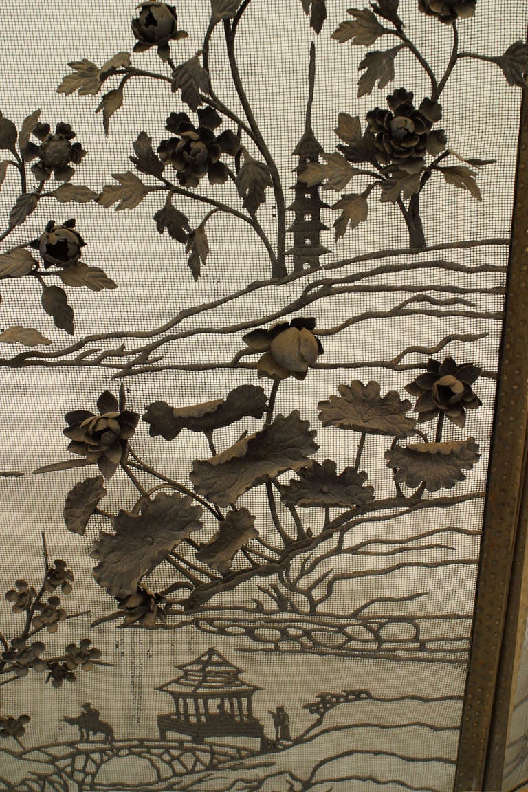 English Arts and Crafts movement fire screen composed of wrought iron and divided into three sections. The screen's metal mesh palette is covered in a three-dimensional iron filigree floral design including Asian themes such as pagodas, mountains,