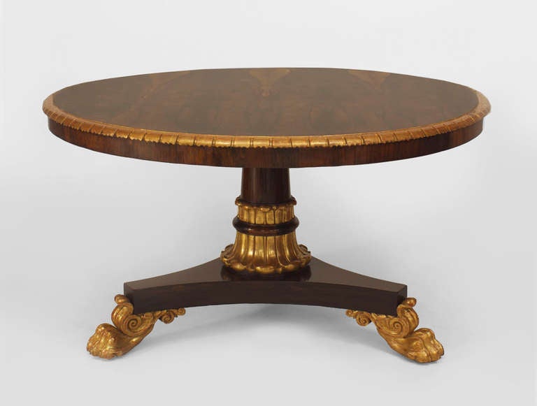 19th c. English George IV round rosewood center table featuring decorative carving and gilding at its edge, its turned acanthus-form pedestal, and its claw-foot tripartite base.