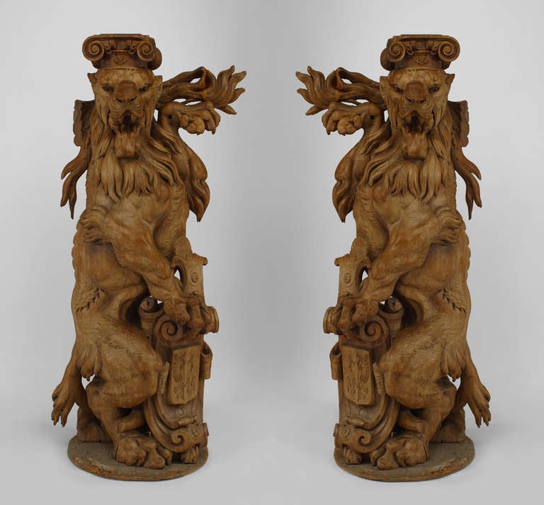 Pair of large hardwood pedestals carved in the form of lions rampant crowned with ionic capitals resting upon cartouche-framed coats of arms.