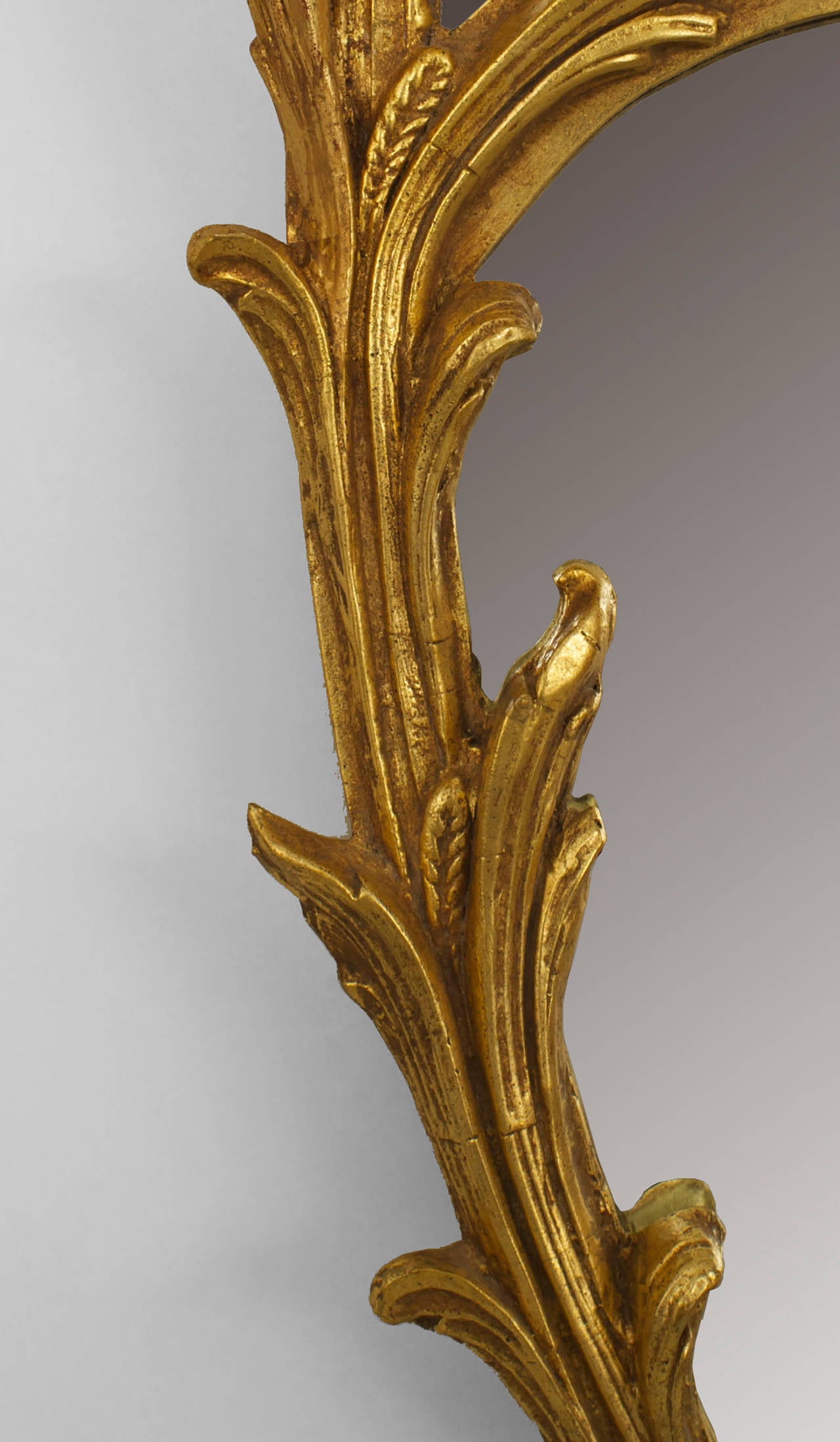 Italian Rococo-style (20th Century) oval-shaped gilt wall mirror with a leaf carved form double frame with a centered beveled mirror and a scroll pediment top.
