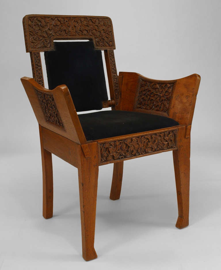 Nineteenth century Burmese style teak club chair with carved arms and a black velvet upholstered seat and back panel.