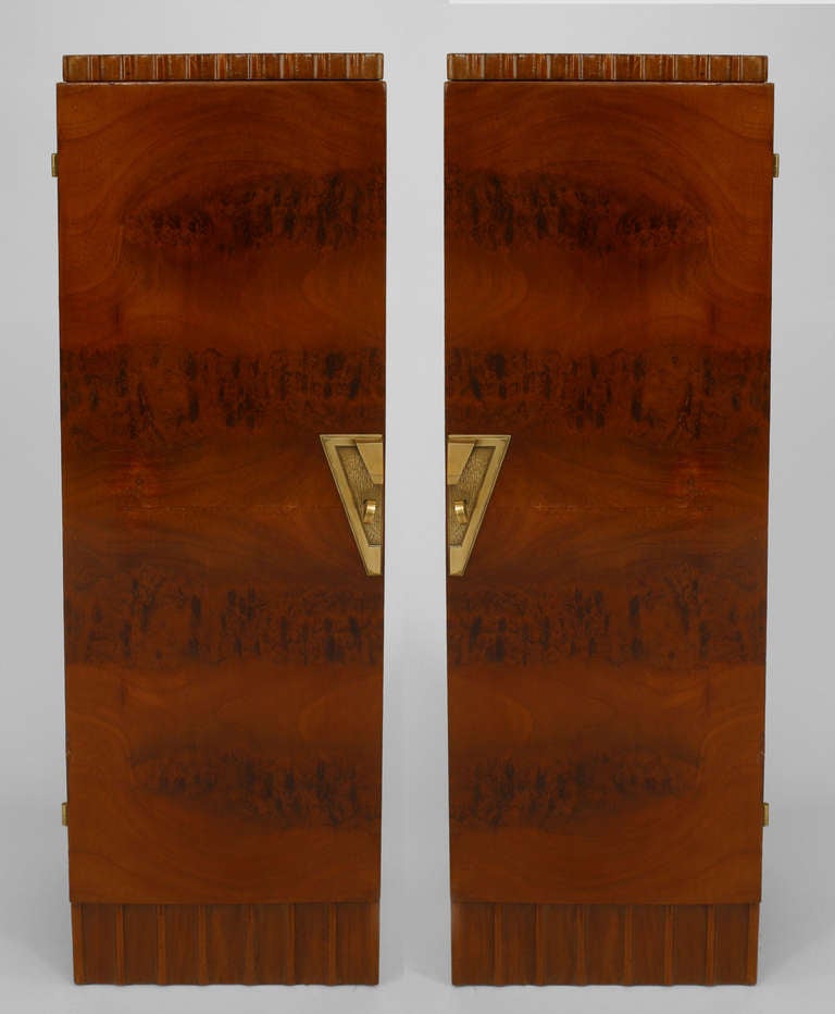 Pair of French Art Deco mahogany veneered pedestal cabinets with fluted tops and bottom edges on either side of front doors finished with bronze geometric key plates that together form a trapezoidal keystone shape.