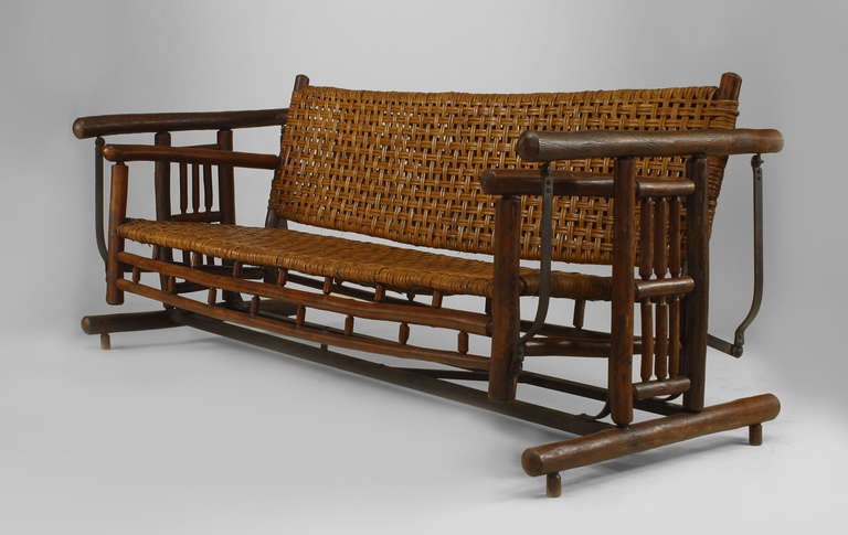 Bearing the brand of the Old Hickory Company of Martinsville, Indiana, this large rustic settee porch glider features a woven seat and back and is supported on a wood and metal spindle design frame.