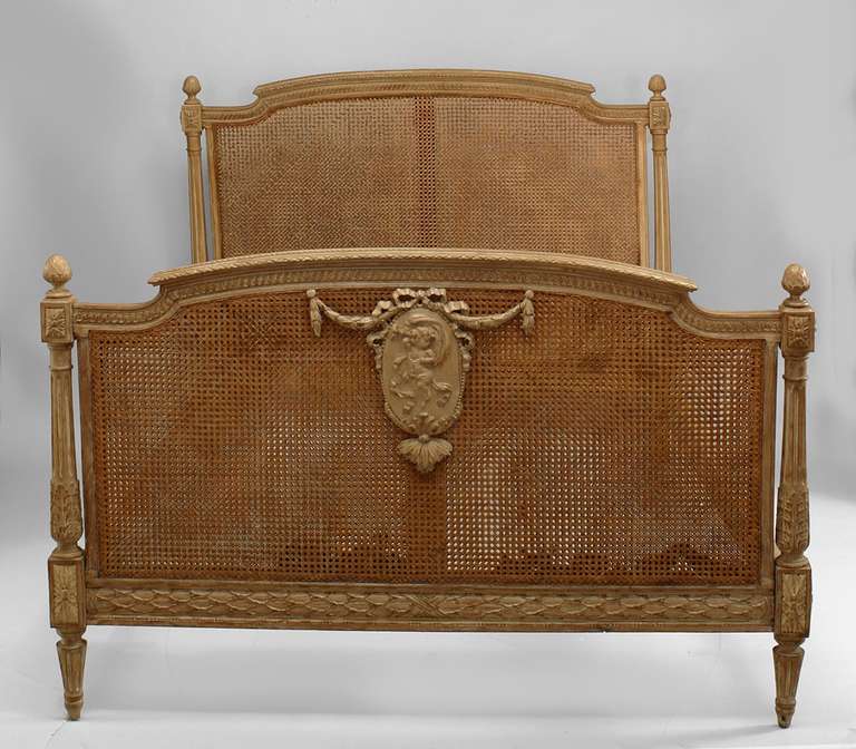 French Louis XVI style full sized bed composed of cane panel trimmed in stripped carved wood. The footboard features a ribbon top footboard medallion carved with a cherub swathed in cloth.