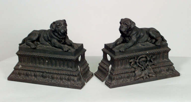 Pair of 19th century English wrought iron andirons in the form of mastiff dog figures reclining upon decorative plinths.