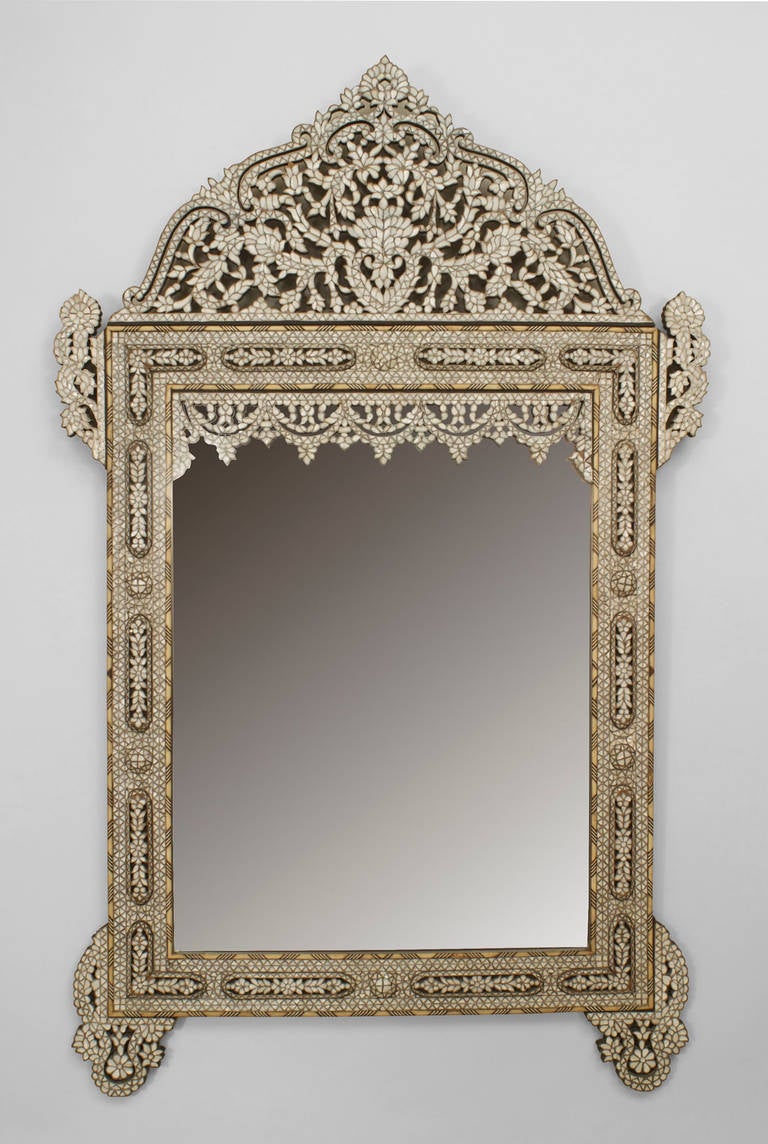 Twentieth century Middle Eastern Syrian or Moorish style vertical wall mirror inlaid with geometric designs of mother of pearl, ebony and bone. The piece features repeated floral filigree decoration, visible at its bold pediment, four corners, and