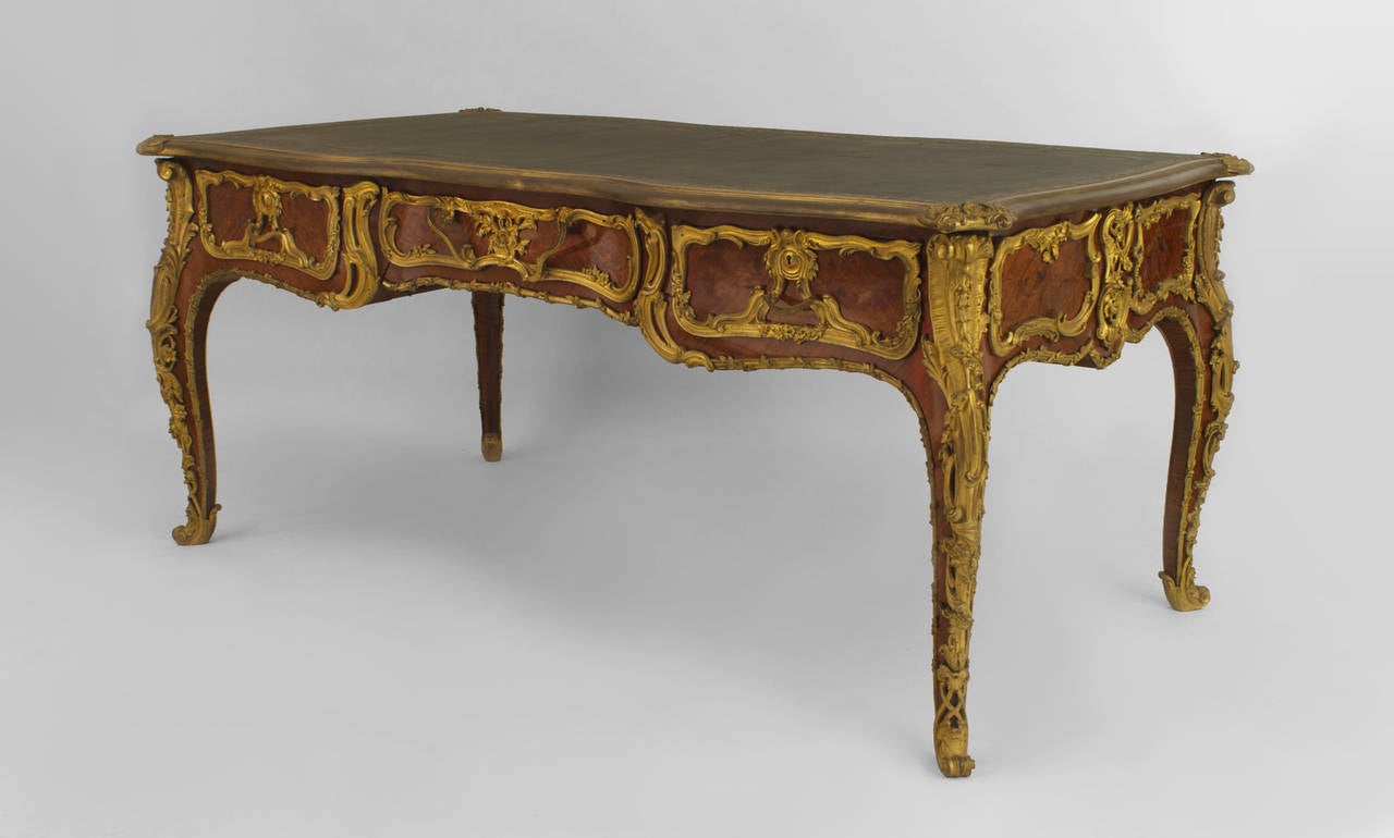 Nineteenth century French Louis XV style kingwood desk decorated with ornate bronze trim and inlaid drawers beneath a dark green top with gold trim.