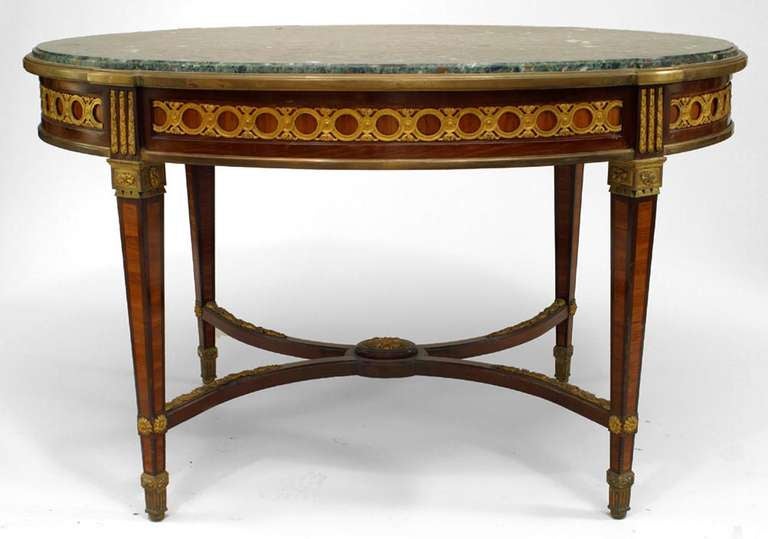 French Louis XVI style (19th Century) mahogany and satinwood oval center table with bronze trim, green marble top, and stretcher.

