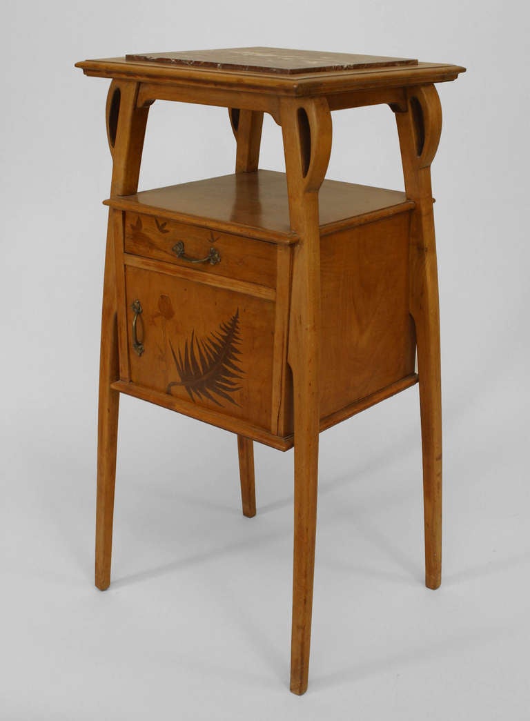 Attributed to French Art Nouveau designer LOUIS BROUHOT, this tapered four-legged bedside commode is composed of maple and features a front drawer and door inlaid with foliate motifs beneath a shelf and brown marble top.