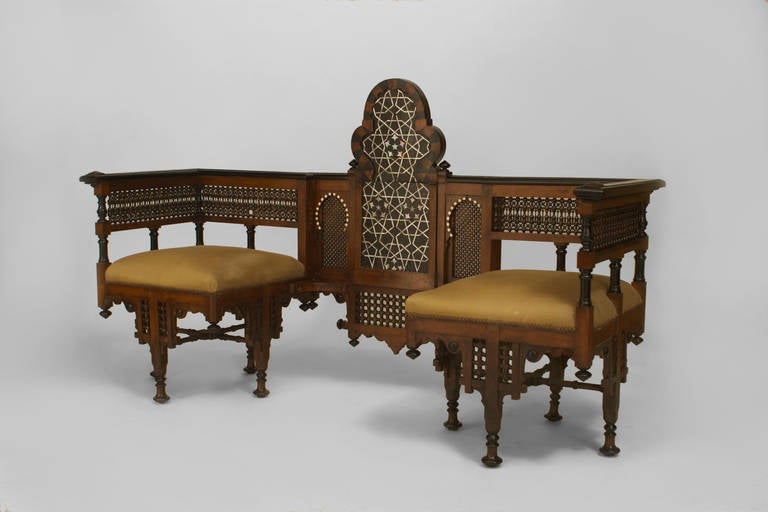 Turn of the century Moorish style conversation loveseat. Two opposing upholstered square seats are supported by a traditional middle eastern spindle and ball frame, which is inlaid with ebony and bone and carved with architecturally-inspired motifs,