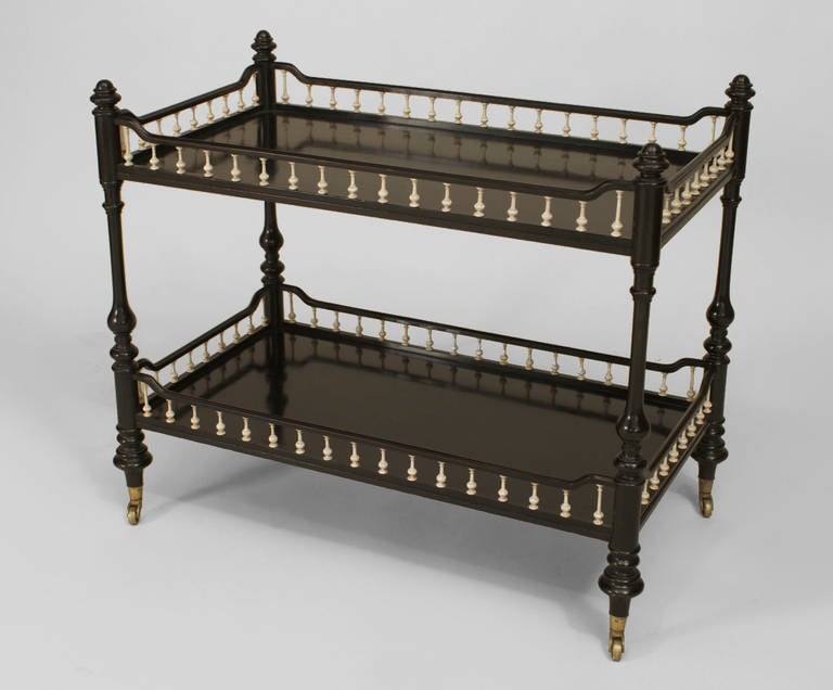 Bearing the label of Howard & Sons, this mid-nineteenth century Anglo-Indian rolling bar cart is composed of ebonized wood and features two shelved tiers, each enclosed by a carved faux ivory spindle gallery.