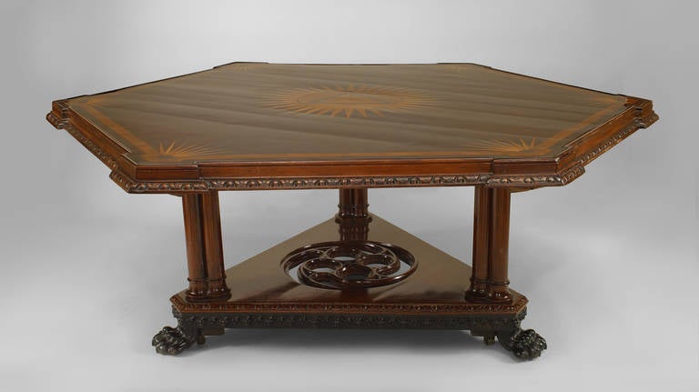 English Regency (circa 1850s) mahogany 6 sided center table with carved apron & satinwood inlaid sunburst center & edge supported on 3 columns & triangular filigree platform.
