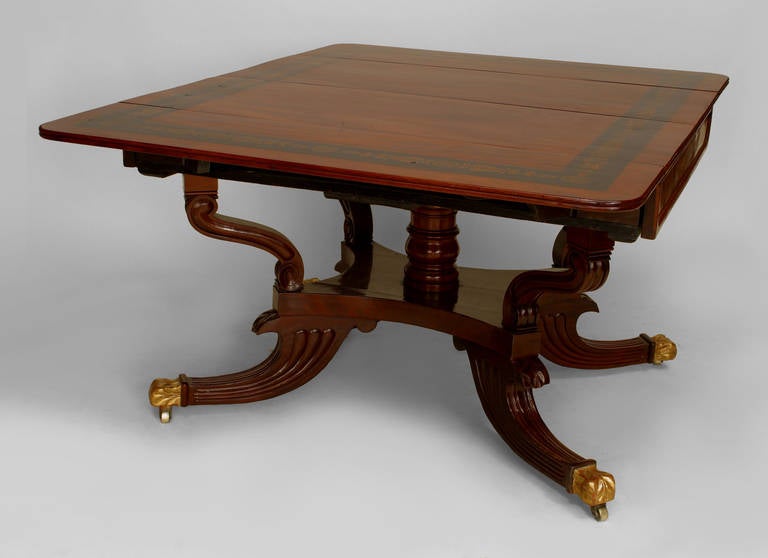 Early nineteenth century English Regency gilt trimmed mahogany dining table with a painted foliate banded top resting upon a turned column pedestal base with four reeded legs finished in brass castors.