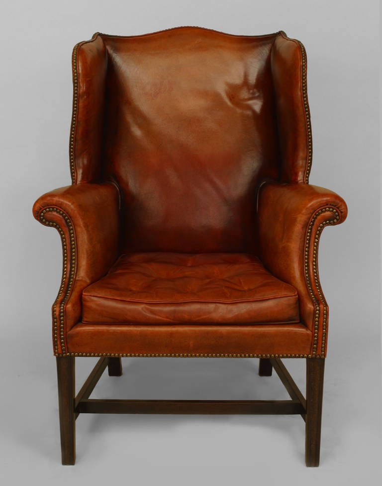 Turn of the century Georgian style rust leather wing chair finished with nail heads, four square legs, and a box stretcher.