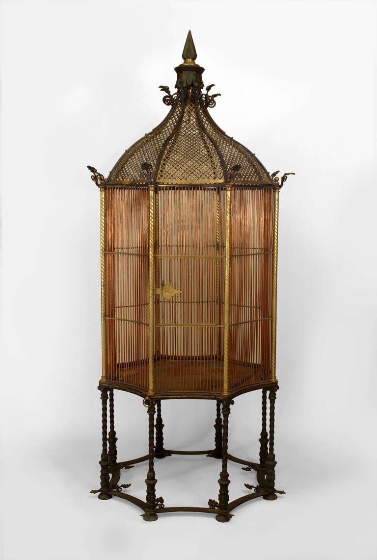 Nineteenth century English monumental birdcage composed of bronze and copper bars arranged in an octagonal form and crowned with a pierced gilt dome and finial top, all mounted upon a base of eight conjoined swirled iron legs. The piece holds the