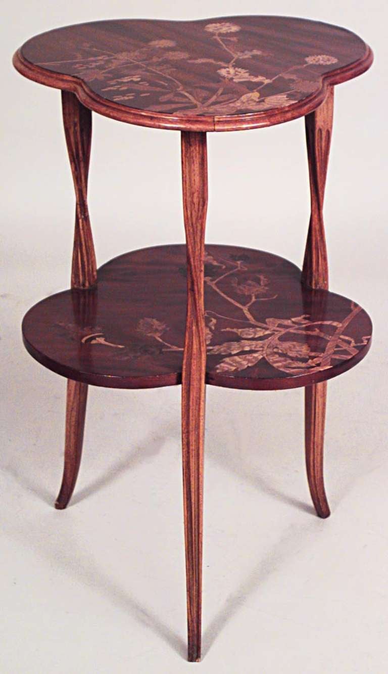 Attributed to French Art Nouveau designer Louis Majorelle, this mahogany end table features a clover-shaped top and lower shelf both inlaid with a floral design and supported by three twisting, vine-like legs.