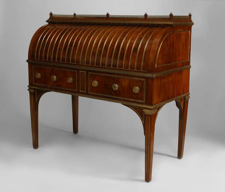 Russian mahogany roll top desk with a brass gallery top and brass handles and trim. The piece rests upon four legs and features an interior with a pull out leather writing surface in front of ten drawers and four ebonized wood columns.