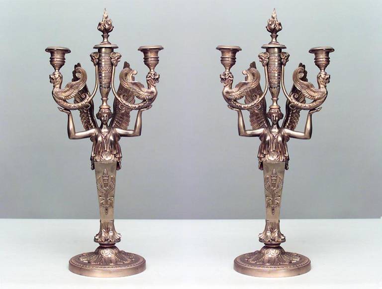 Zwei dreiarmige klassische Kandelaber aus französischer Empire-Bronze, jeder mit einem Karyatidenfuß, der zwei Greifen auf beiden Seiten eines flammenden Feuerzangenbowle aufrichtet.