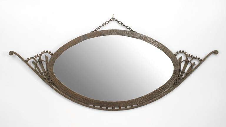 Attributed to French Art Deco designer Raymond Subes, this wall mirror is oval in form and encased within a filigreed wrought iron frame suspended from the wall by a small wrought iron chain.

French metalworker Raymond Subes’ illustrious career was
