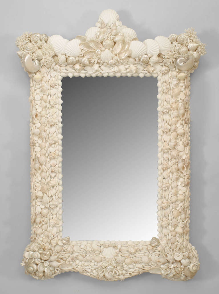 Twentieth century Venetian Grotto style wall mirror featuring a rectangular panel of mirrored glass set within a shaped frame studded with a variety of white seashells and coral fragments beneath a scallop shell pediment top.