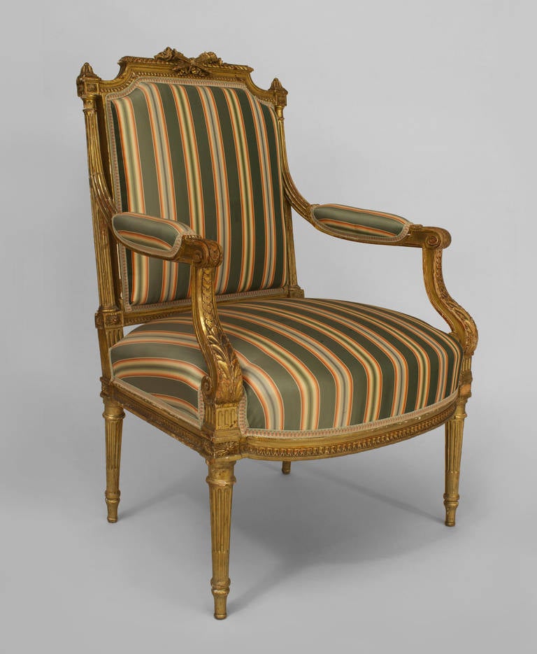 French Louis XVI style (19th Cent) gilt open arm chair with carved crossed torches on back crest and upholstered in green stripe damask.
