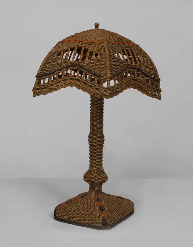 American Art Deco table lamp composed of natural wicker with black and orange trim. The lamp rests upon a square base and  is sheathed in a scalloped six-sided filigree umbrella form shade, which measures eighteen inches in diameter.