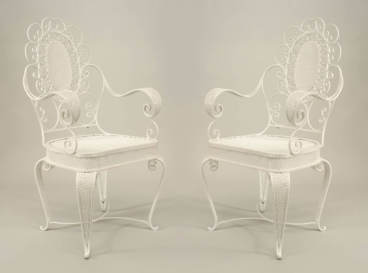 Pair of twentieth century Victorian style white painted iron open arm chairs with filigree patterned legs, seats, and aprons, with back panels centered with scrolls.