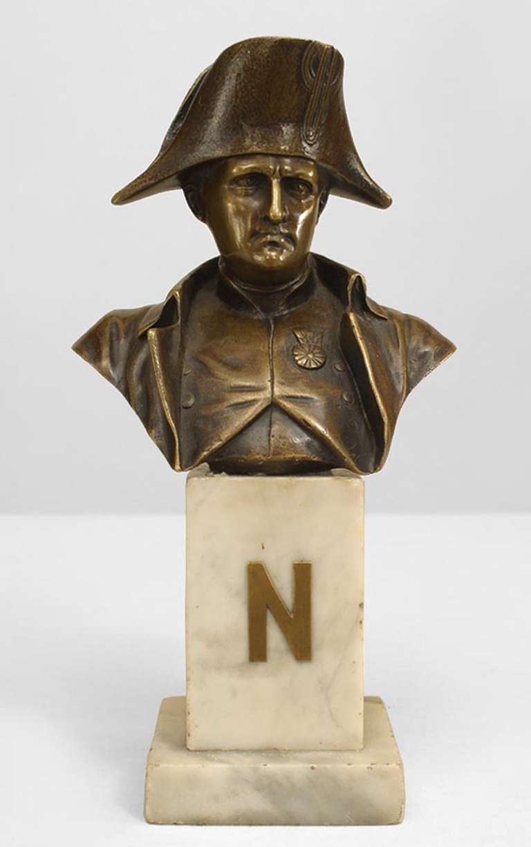 Small turn of the century French Empire style bronze bust representing Napoleon's uniformed likeness propped upon a white marble pedestal base adorned with a bronze letter 