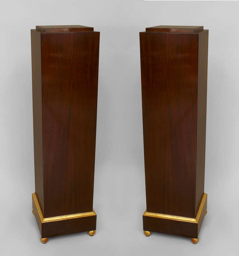 Pair of Art Deco pedestals composed of mahogany carved in the form of two solid plinths, each with beveled gilt trimmed box bases resting upon four spherical gilt feet. Top measures 9.25