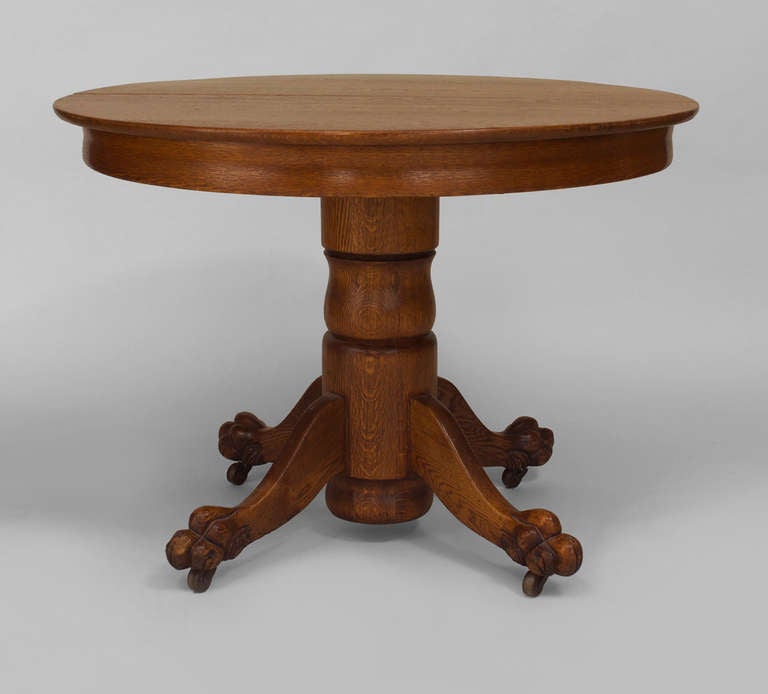 1920's American dining table composed of oak with a round top and uncarved apron resting upon a tiered pedestal base and four clawfooted legs.