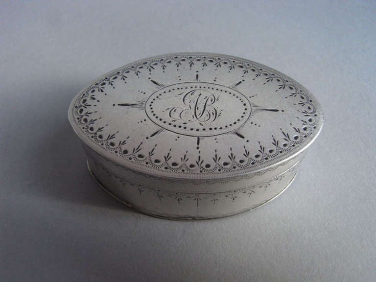 The Nutmeg Grater is oval in form and is decorated on the sides and cover with various crisp bright cut designs. The cover displays a central cartouche engraved with contemporary script initials, surrounded by a sunburst motif. The base is