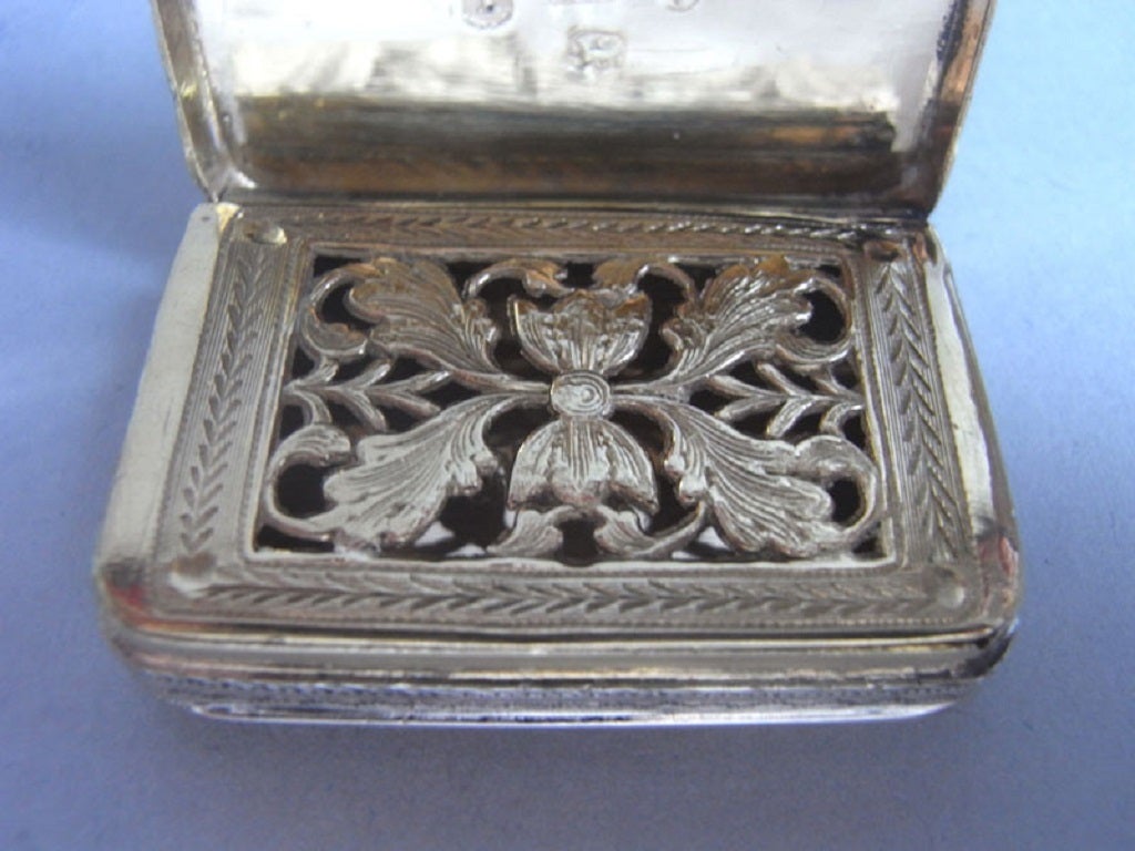 The Vinaigrette is broad rectangular in form and is engraved on the cover and base with very unusual scroll work designs on a scratch engraved ground, as well as neoclassical oval medallions containing flower heads. The sides are decorated with