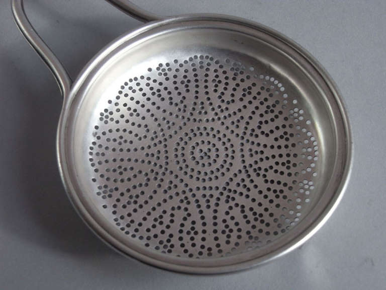 The strainer has a circular bowl with raised rim. The centre is pierced with entwined circular designs and roundels. The arched side handle is decorated with reeding and the side clip is engraved with a set of contemporary initials.