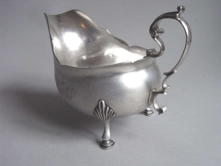 The Sauceboat stands on three hoof feet which are attached to the main body with stylized shell mouldings. The elongated main body has a shaped rim and pronounced pouring spout. This piece is engraved on each side with a set of contemporary script