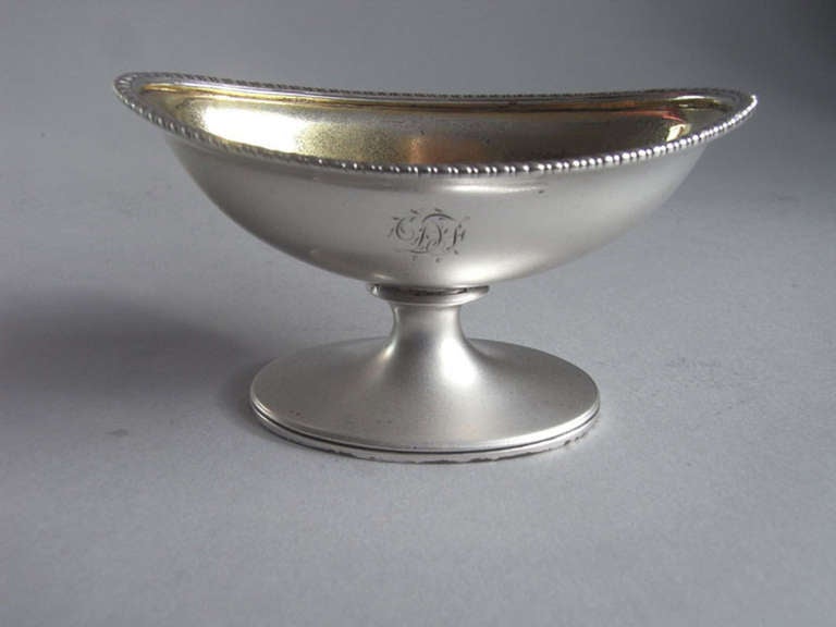 The salts are boat shaped in form with an oval pedestal foot which is decorated with reeding. Both have a gadrooned rim, fine interior gilding and a set of contemporary initials engraved on the front of the main body. One salt cellar was made in