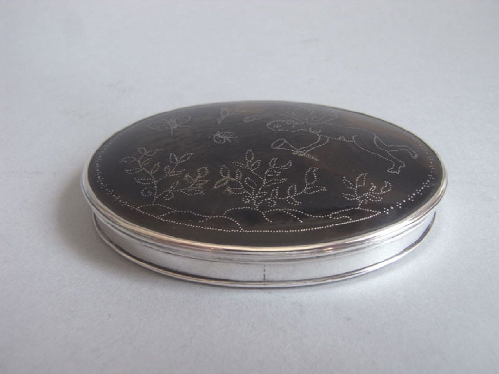 The Snuff Box is of an oval form with silver sides and mounts and a stand away hinge. The base is inset with a plain tortoiseshell panel and the cover displays a most unusual panel decorated with fine bead work depicting a cherub, holding a torch,