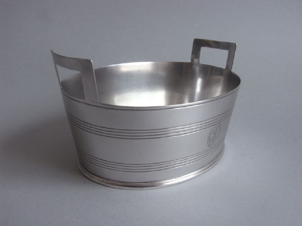 The Butter Tub is unusually modelled as a coopered Tub with two pierced side carrying handles. The sides are decorated with reeded bands, to simulate the metal horizontal bands. The front is also engraved with a contemporary Crest surrounded by a