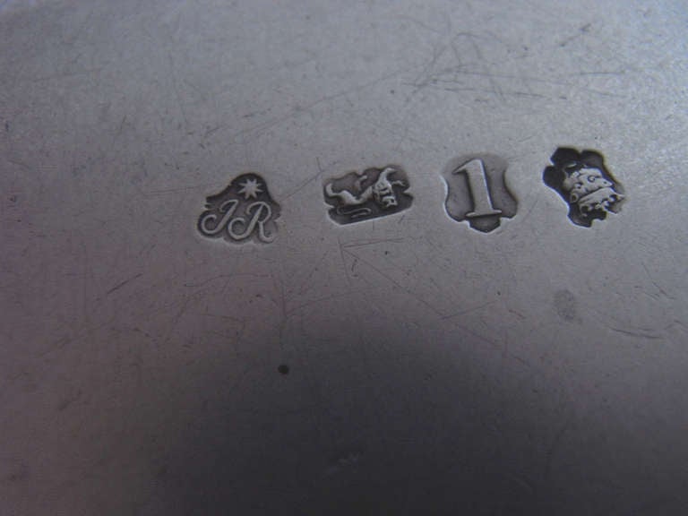 The Salvers stand on three hoof feet and display a raised scroll border interspersed with shells. The centre of the salvers is engraved with a Rococo scroll, shell and strapwork cartouche, also displaying foliate sprigs. The centre of the cartouche