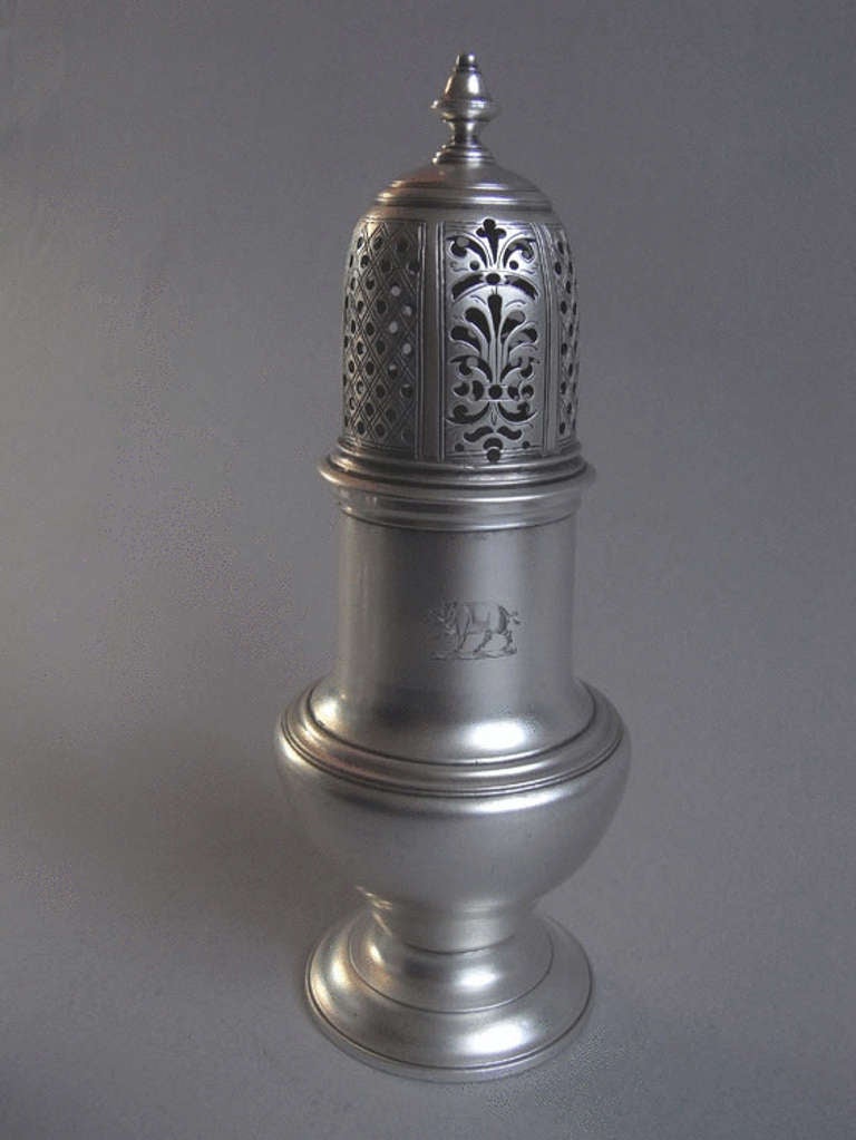 The Casters are baluster in form and stand on cast spreading feet. The pull off covers terminate in a cast bell finial and are pierced with scroll work and plain roundells, as well displaying trellis work engraving. The large caster would have been