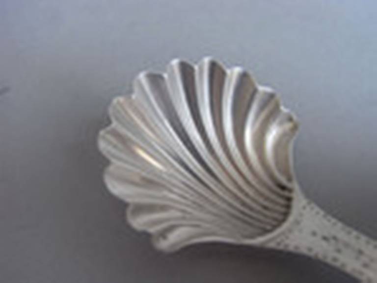 The Caddy Spoon has a scallop shell bowl and the curved handle is decorated with bright cut and prick dot designs. The top of the stem is also engraved with a set of contemporary script initials. A near identical example is illustrated in 