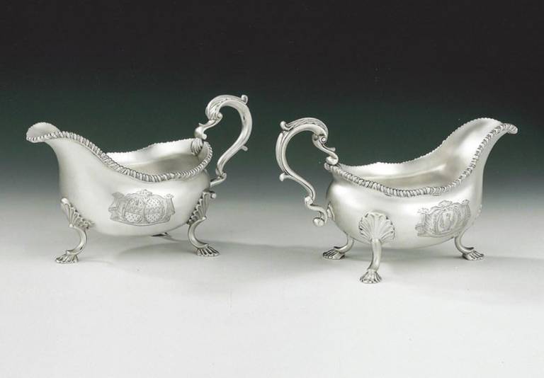 The sauce boats stand on three scrolls legs with shell feet and shell mouldings where they are attached to the main body. The main body has a beautiful slightly baluster form with a shaped gadrooned rim. The scroll handle is decorated with leaf