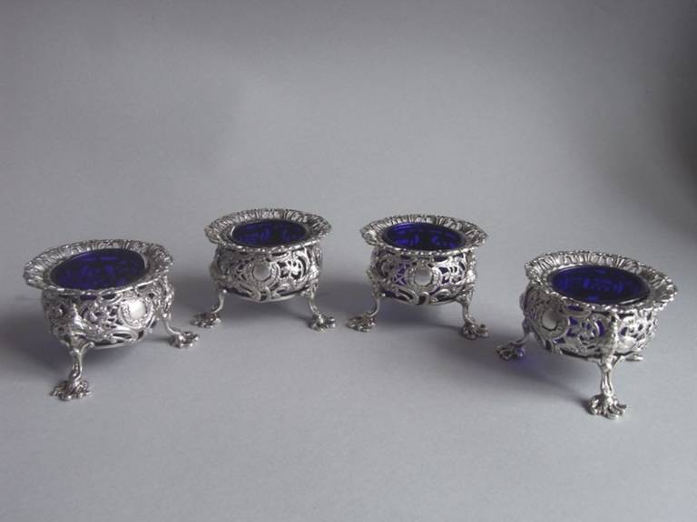 The Salt Cellars are cast and stand on three unusual scroll legs with shell feet and China man mask mouldings where they are attached to the main body. The flared wavy rim is unusually pierced with arch work and the baluster sides display unusual