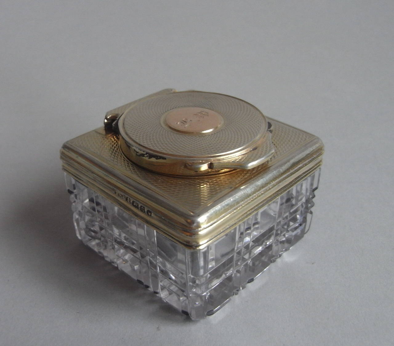 The inkwell is of square form with attractive engine turned silver gilt mounts. The glass is deeply cut and the hinged cover displays a gold disc cartouche engraved with a set of contemporary initials. This piece is very well marked and is in
